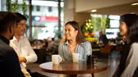 Group of colleagues sitting together having a conversation, gathered around a table with coffee mugs.