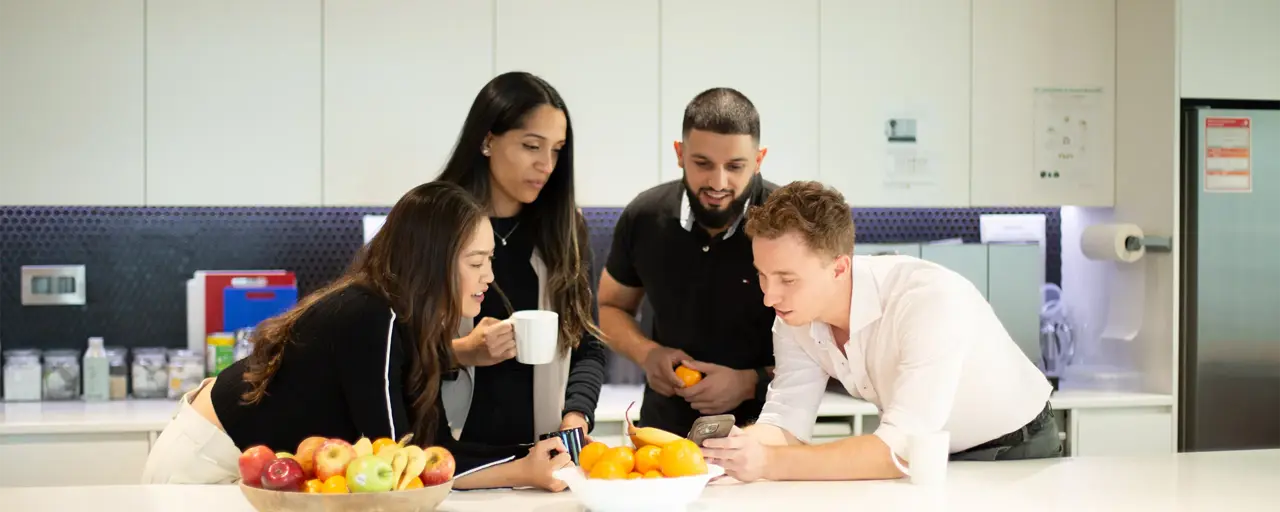 A group of employees having a casual chat in the kitchen with a table with fruit baskets.