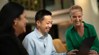 Three colleague gathered around a laptop laughing and engaging in conversation.