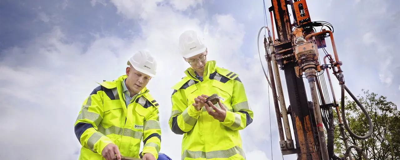 Two men wearing high-visibility jackets and hard hats standing in front of a construction vehicle
