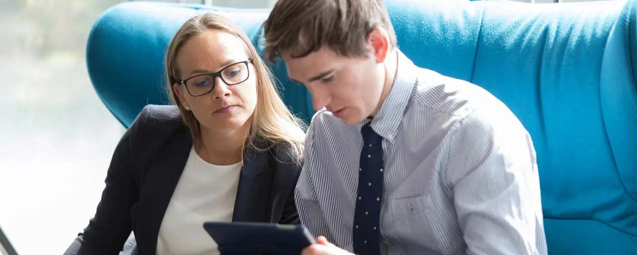 Man and woman sitting on blue chair looking at tablet