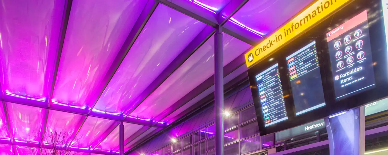 Airport terminal  with purple ceiling and check-in information board