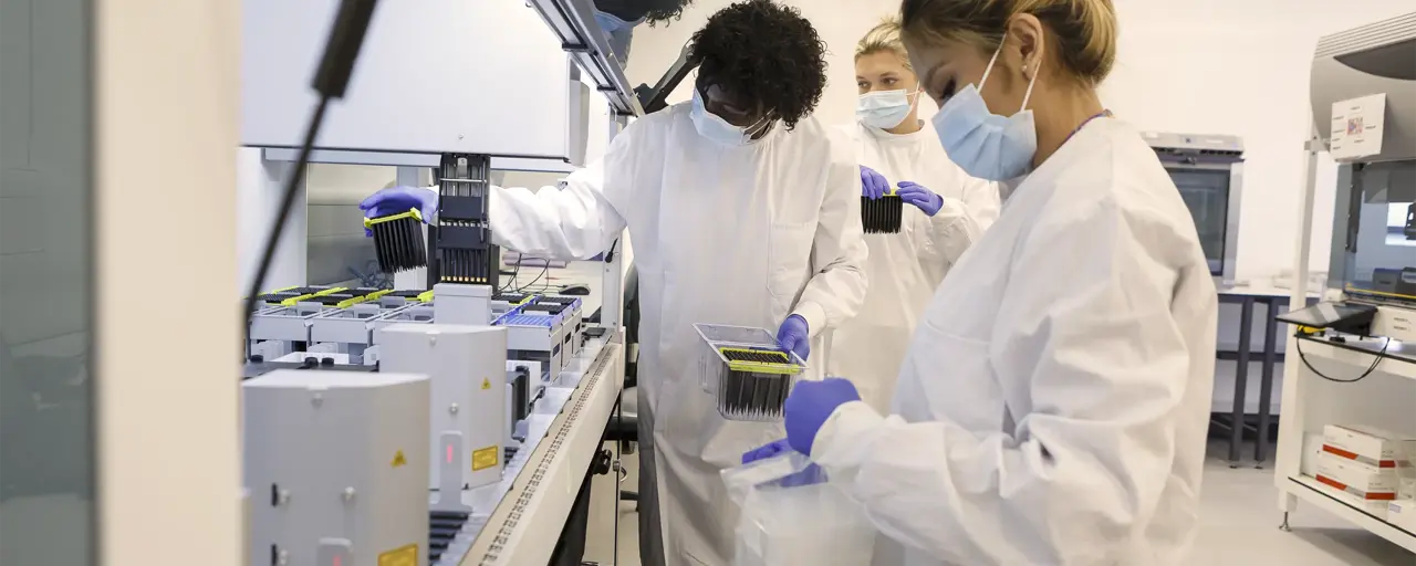 Students in a university science lab with white coats and face masks on working on machine.