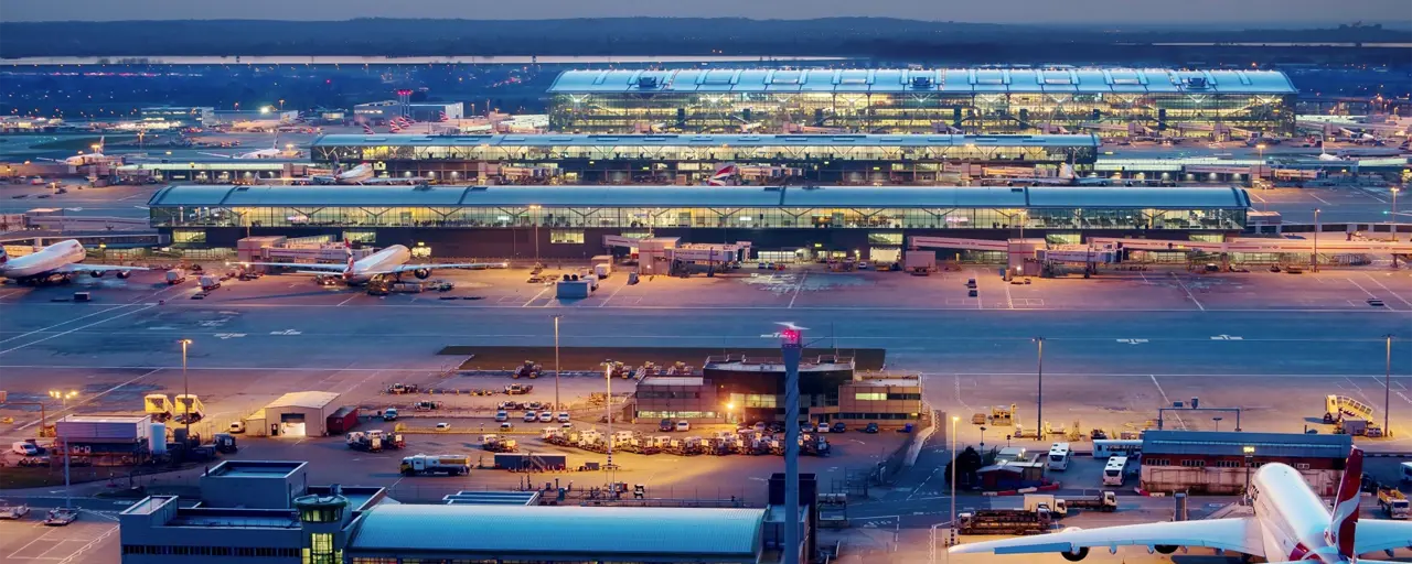 Heathrow airport featuring an airplane, bright lights in the building and orange sunset in the background